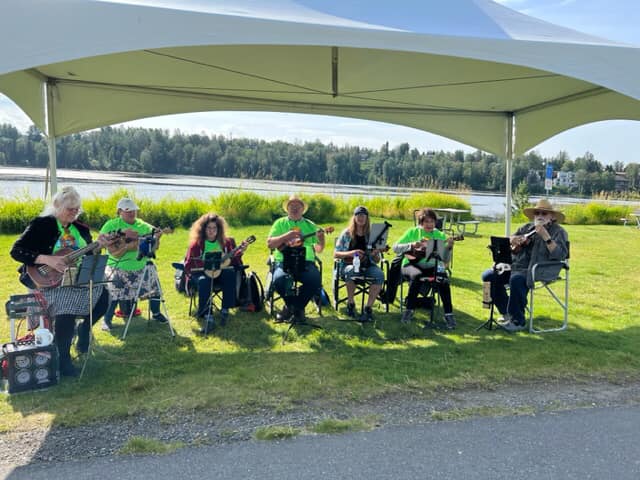 Musicians from the Alaska Jumping Flea Society performing under a tent canopy